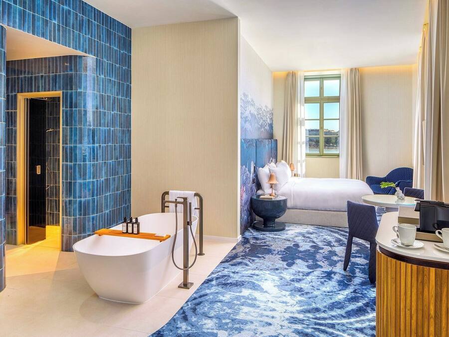 A modern hotel bathroom with a large bathtub, a shower, and a seating area with a table and chairs.