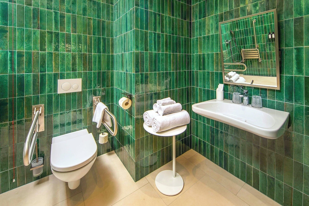 Een badkamer met groene tegels, een wit toilet, een wastafel en een spiegel.