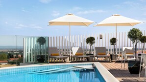 A rooftop pool area with lounge chairs and umbrellas, surrounded by a white fence and glass panels. - Holiday Inn Beja by IHG (Beja)