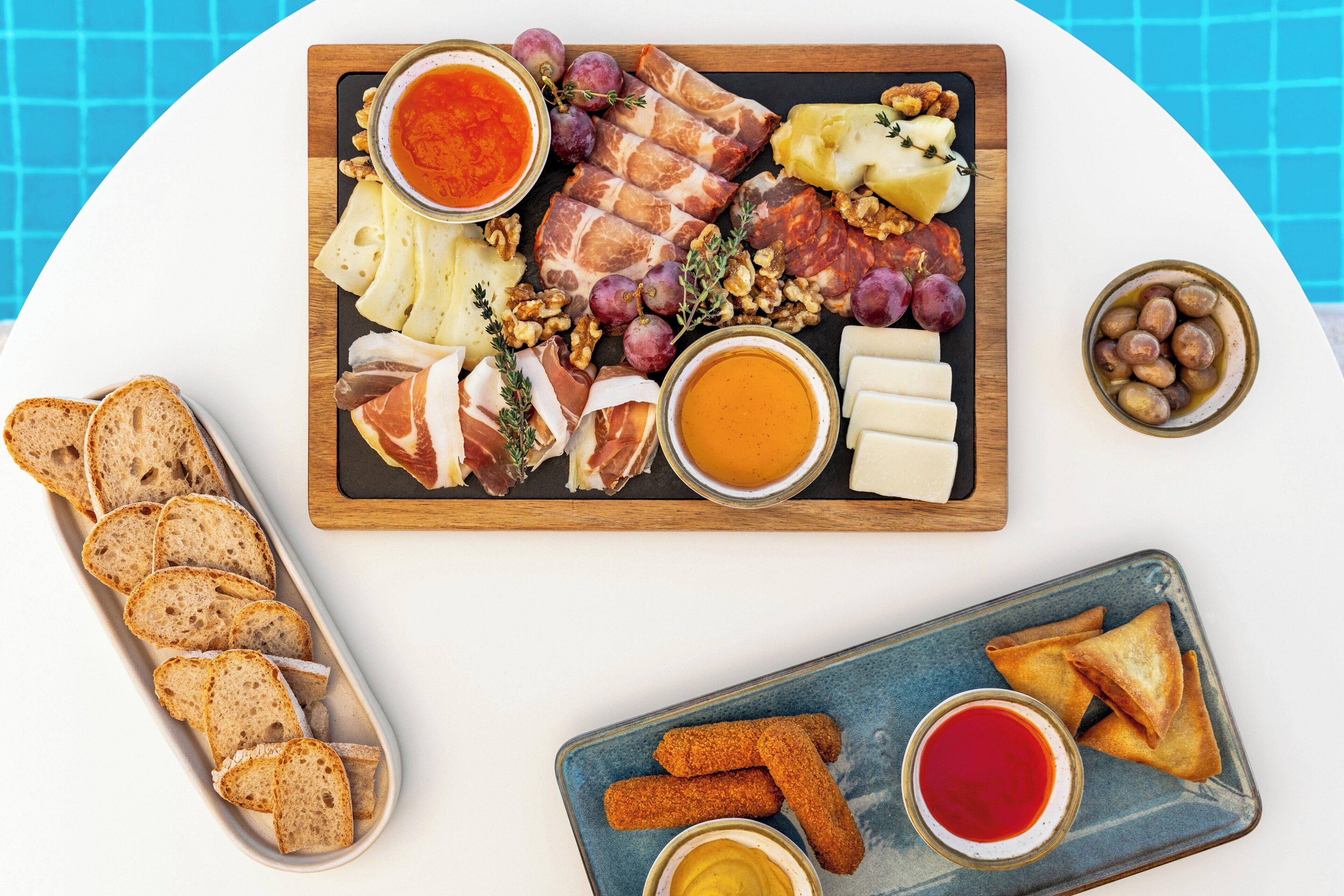 A charcuterie board with various meats, cheeses, and fruits, accompanied by bread and dipping sauces.