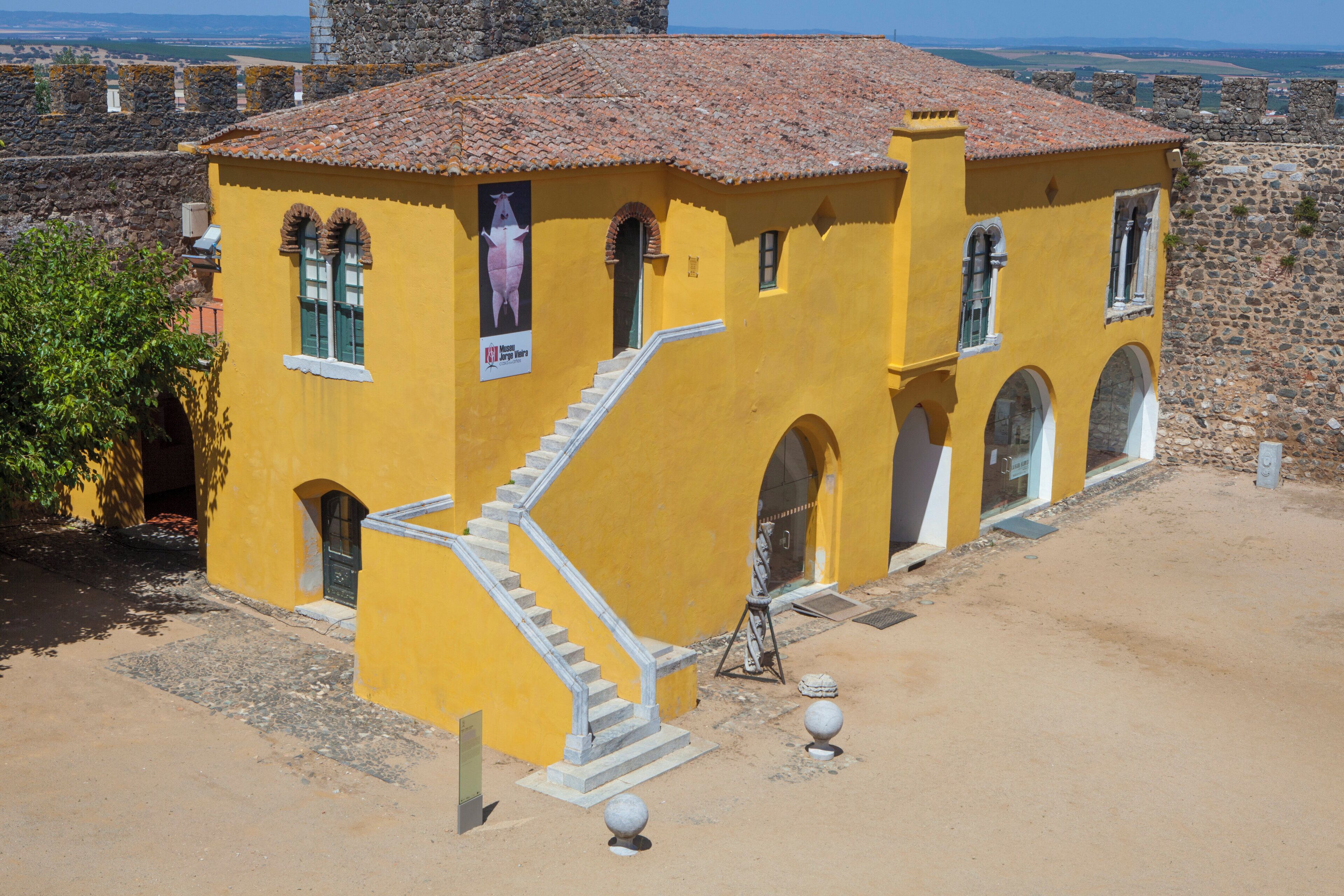 A yellow building with a tiled roof, a staircase, and arched windows.
