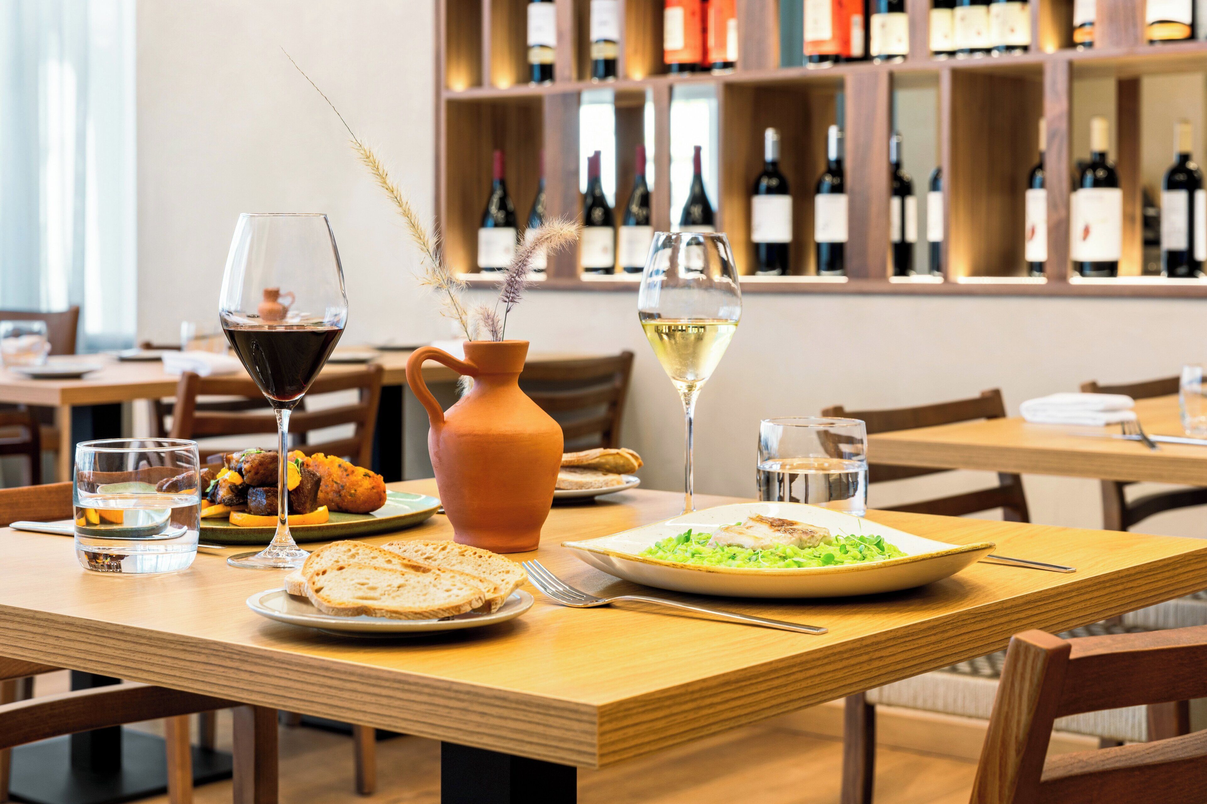 A dining table with plates of food, glasses of wine, and a vase with dried plants.