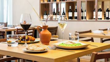 A dining table with plates of food, glasses of wine, and a vase with dried plants.