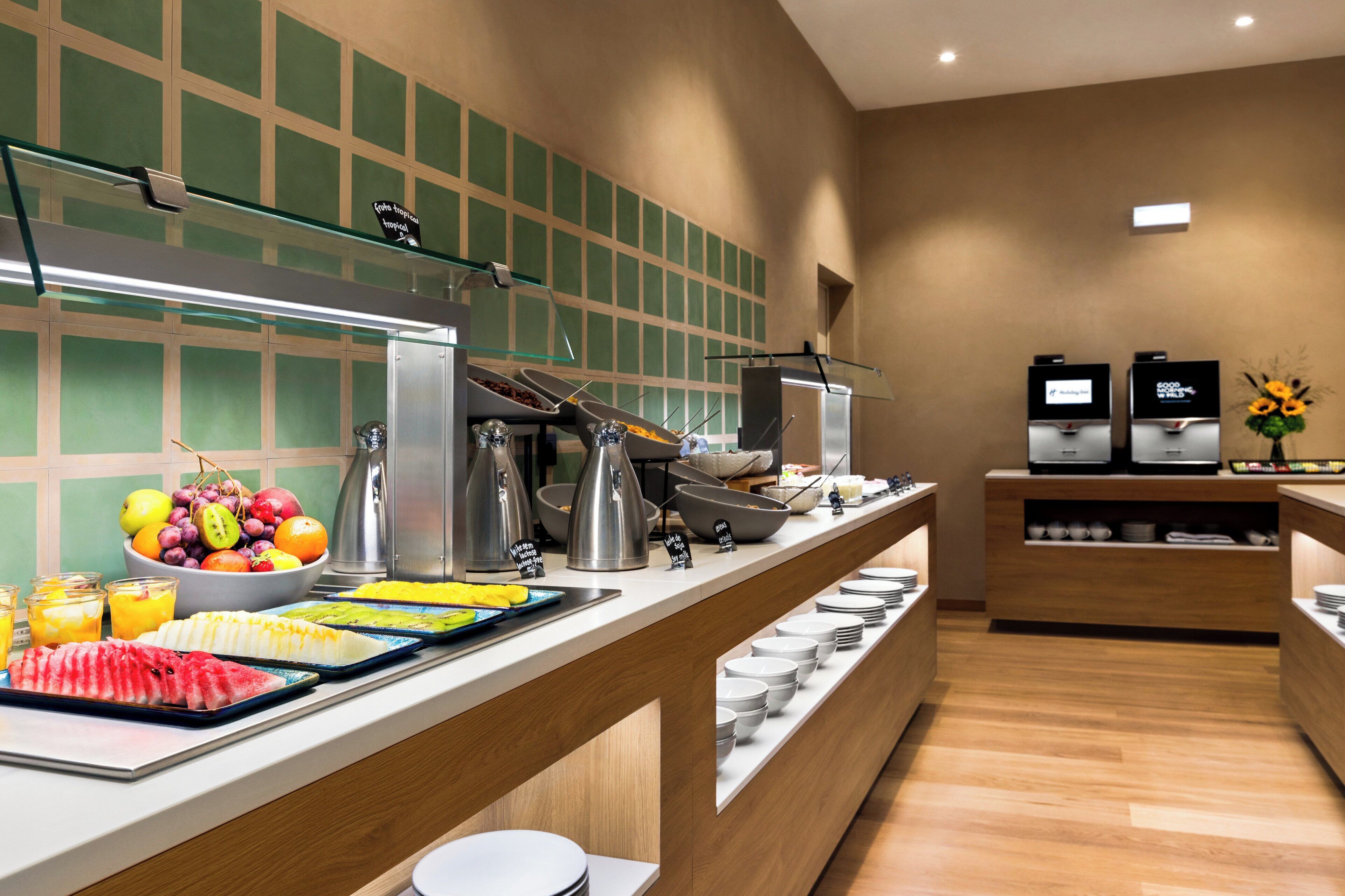 A buffet setup with various food items and beverages, a coffee machine, and a flower arrangement.