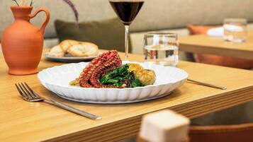 Una mesa de comedor con un plato de comida, una copa de vino tinto y un florero con plantas secas.
