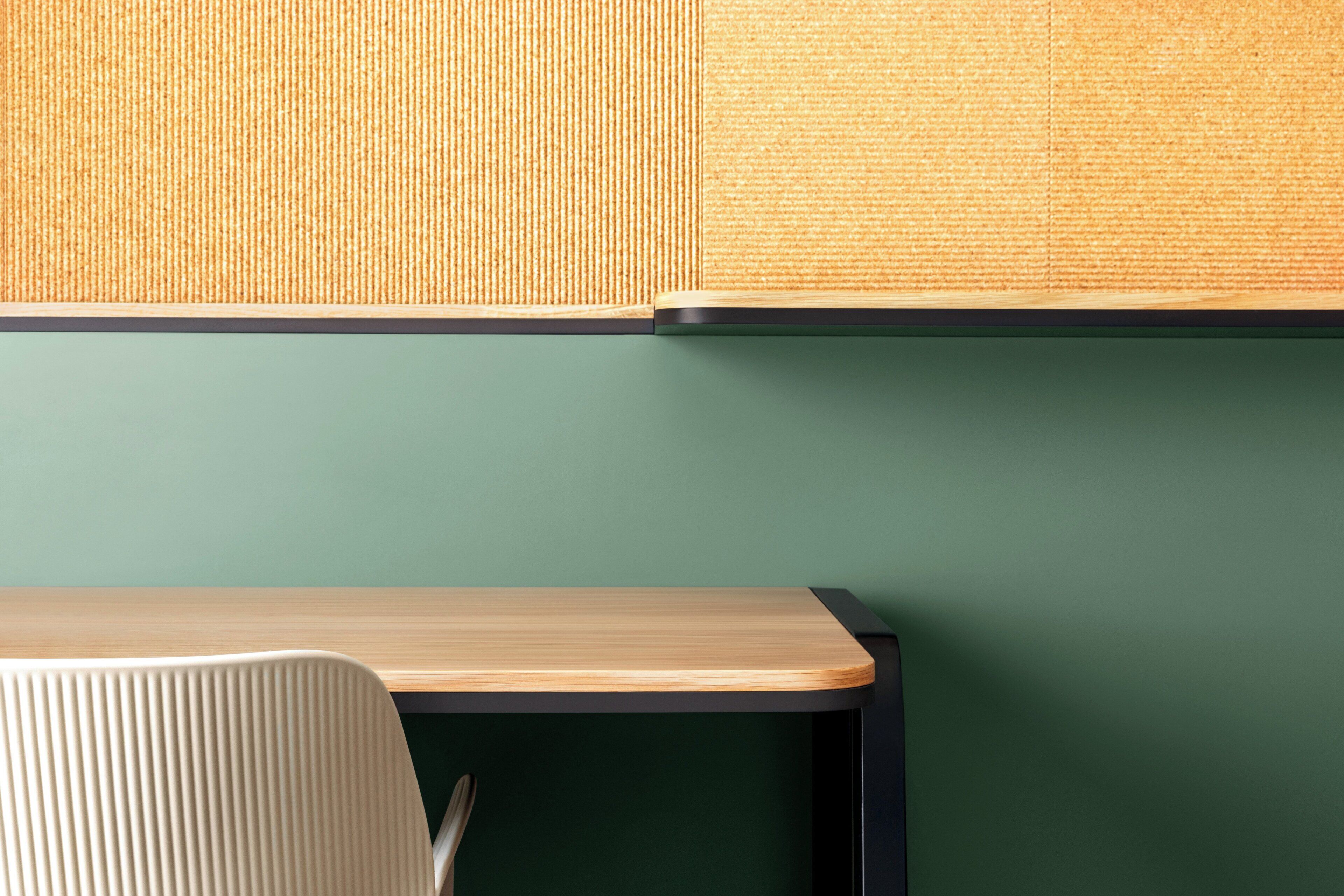 Una habitación moderna con un escritorio de madera, una pared verde y un panel texturizado sobre el escritorio.