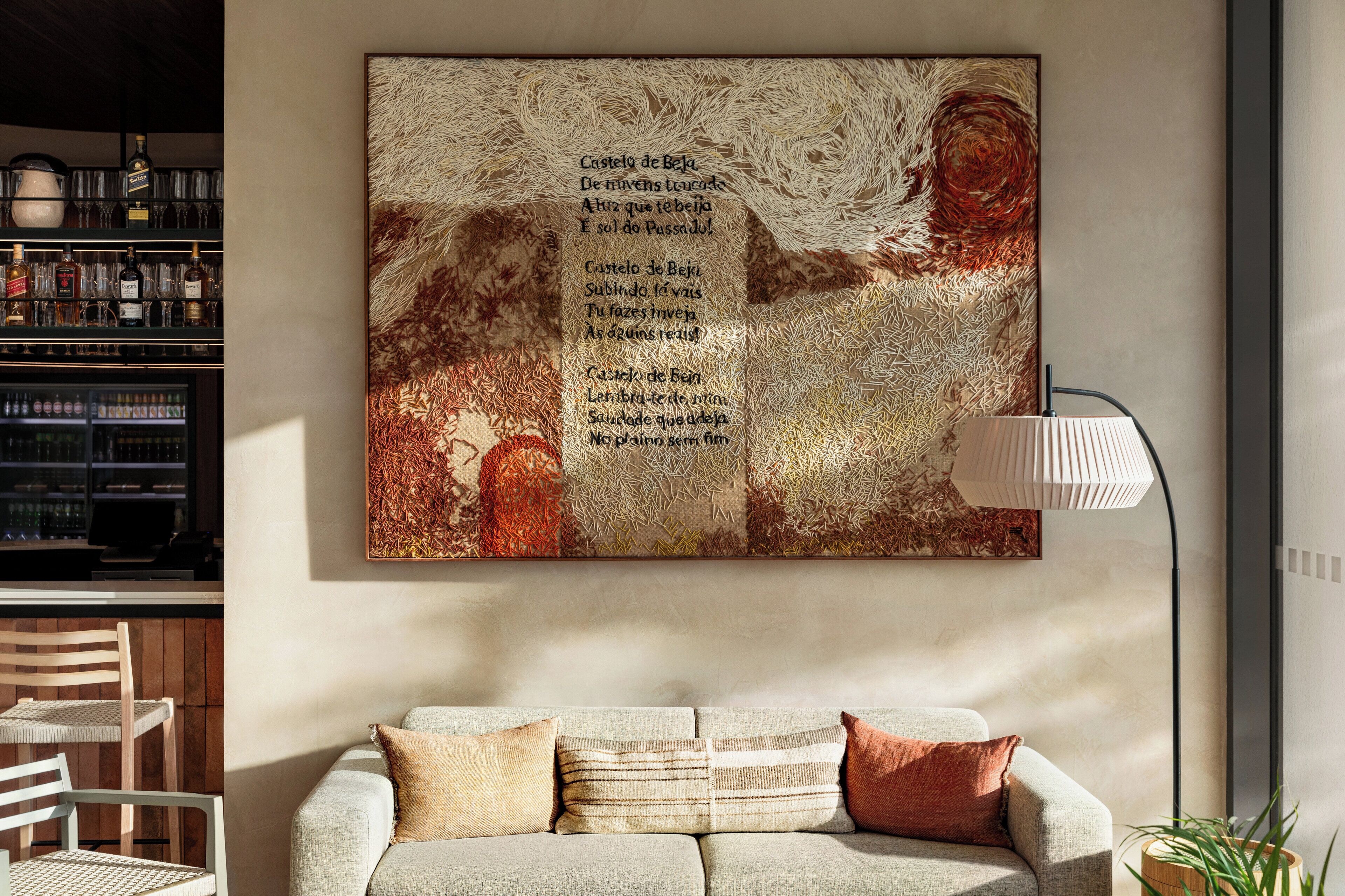 A modern living room with a large abstract painting, a sofa, a lamp, and a bar area with bottles and glasses.