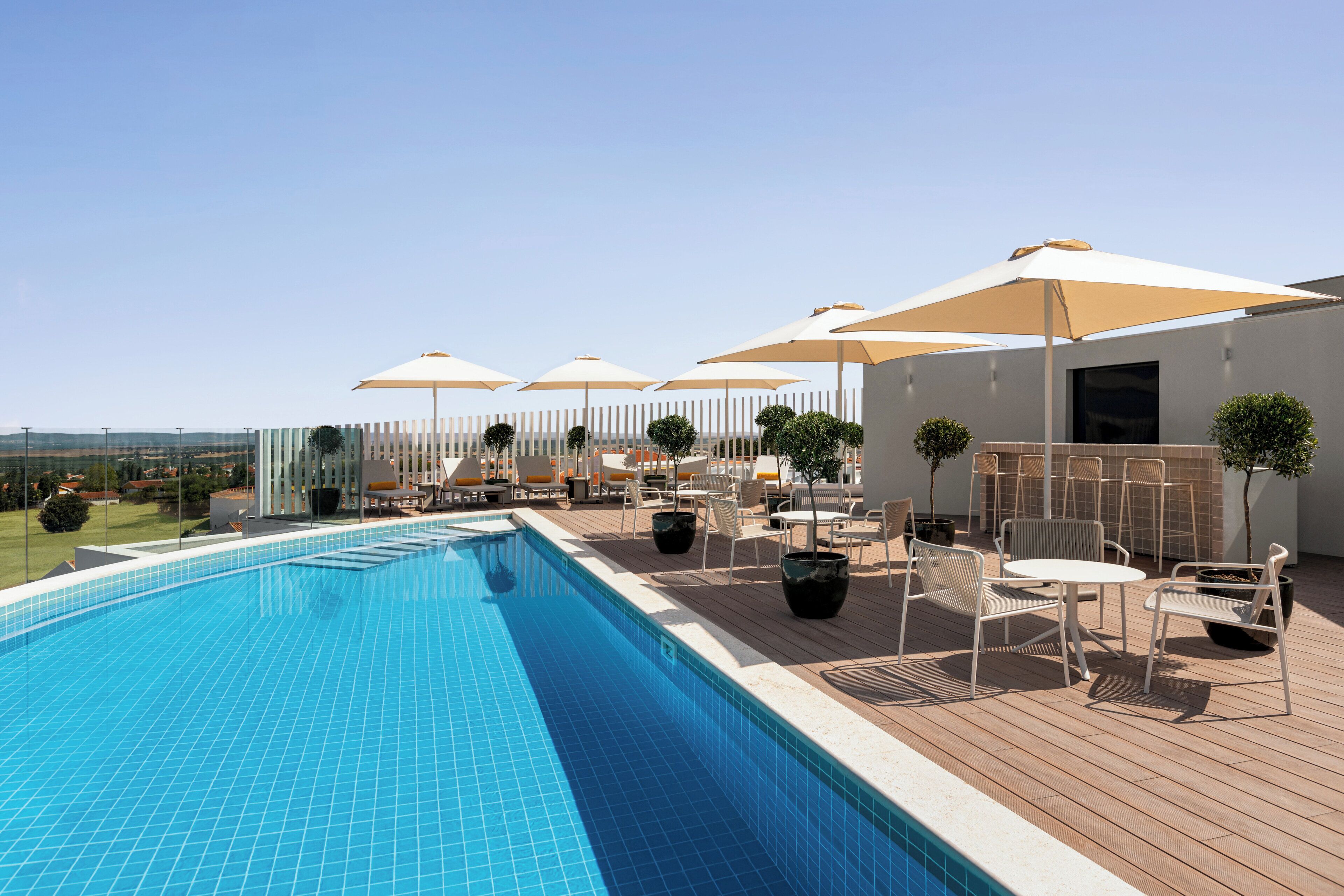 Une piscine entourée d’une terrasse en bois et de plantes en pot, avec des chaises longues et des parasols à proximité.