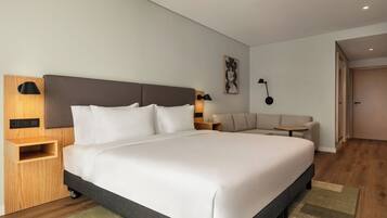 Una habitación de hotel moderna con una cama grande, un sofá, una mesita y una lámpara de pared.