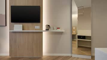 A modern hotel room with a wooden accent wall, a flat-screen TV mounted above a white console, a coffee maker, and a mirror reflecting the room.