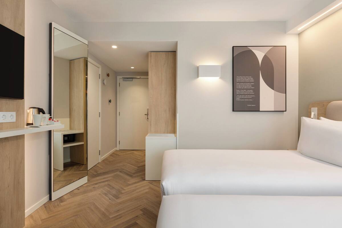 A modern hotel room with a large bed, a bedside table, a mirror, and a wall-mounted artwork.