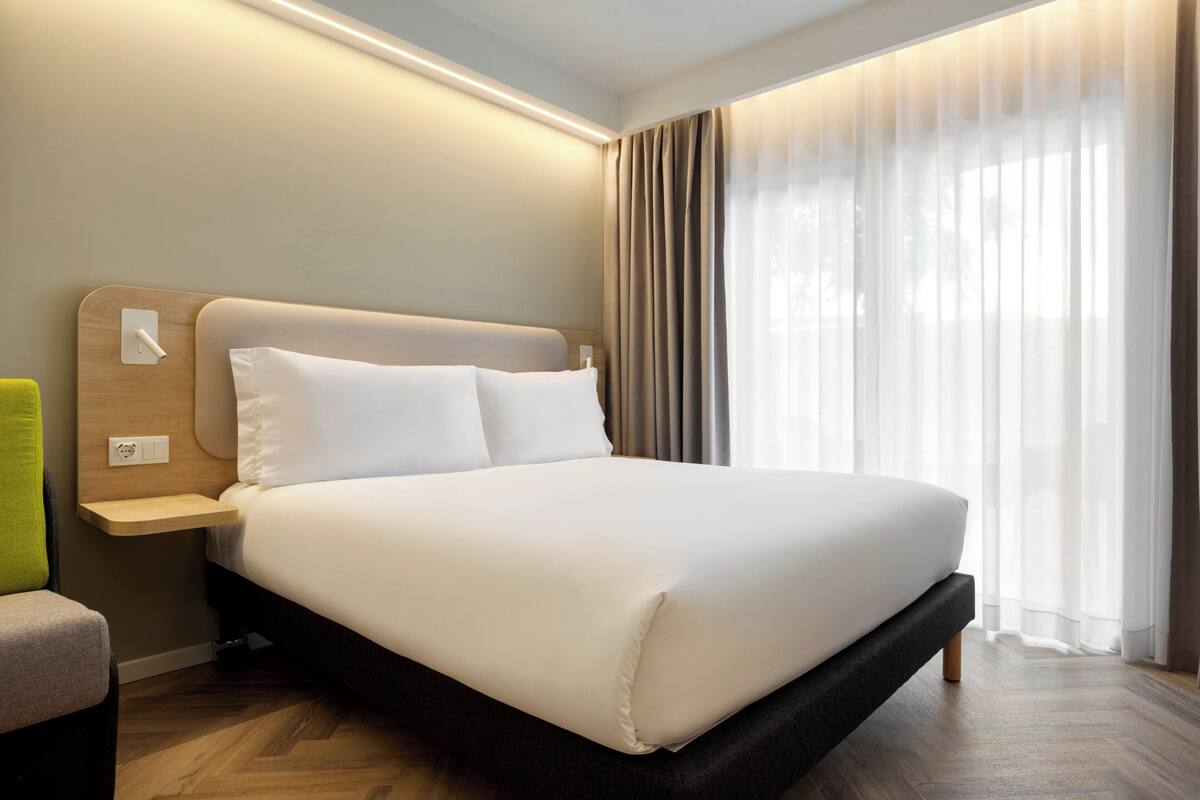 A modern hotel room with a large bed, a bedside table, and a chair.