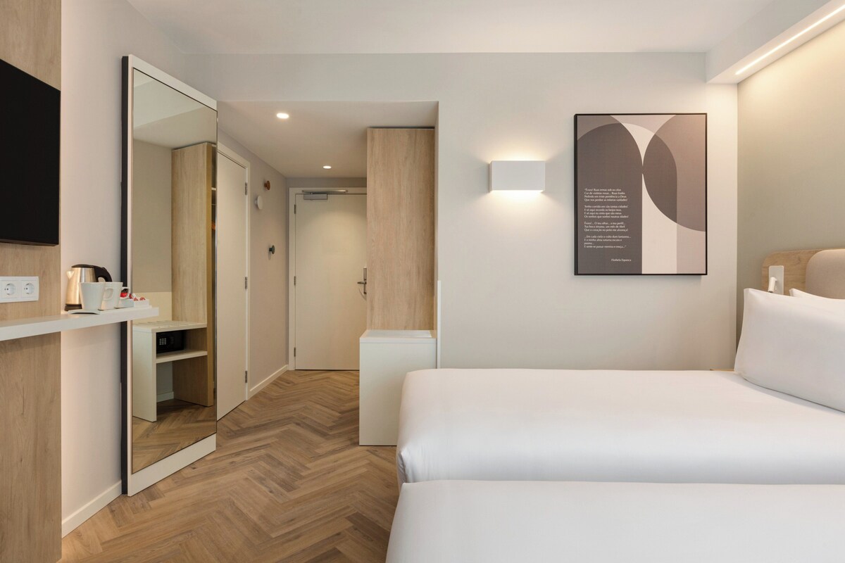 Camera d'albergo moderna con un ampio letto, un comodino, uno specchio e un'opera d'arte appesa al muro.