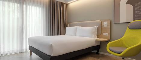 Een moderne hotelkamer met een groot bed, een felgele stoel en een groot raam met dunne gordijnen.