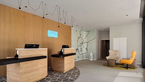 A reception area with two wooden reception desks, a map on the wall, and a seating area with two chairs. - Holiday Inn Express Evora by IHG (Évora)