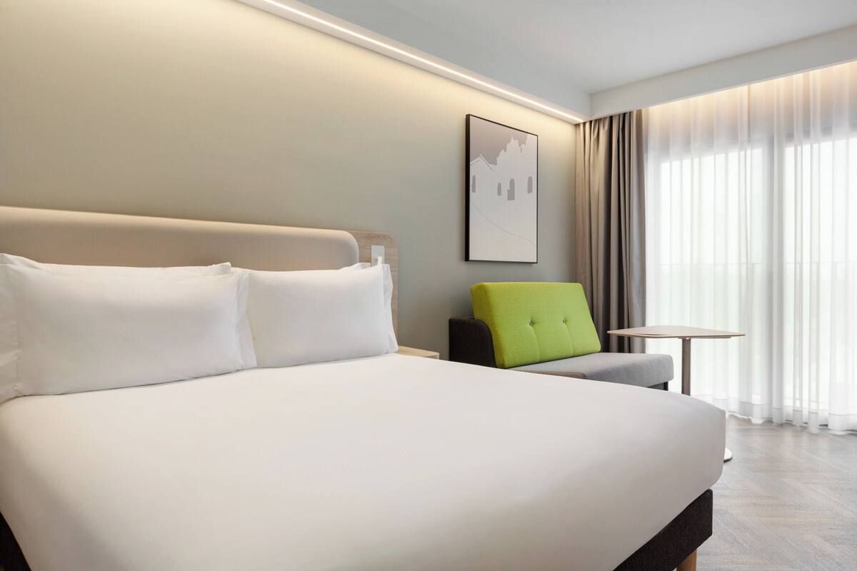 A modern hotel room with a large bed, a small table, and a chair.