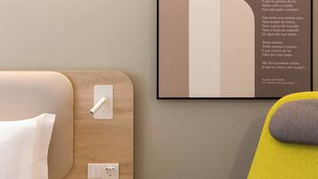 Una habitación de hotel ordenada con cama, mesita de noche y una cita enmarcada en la pared.
