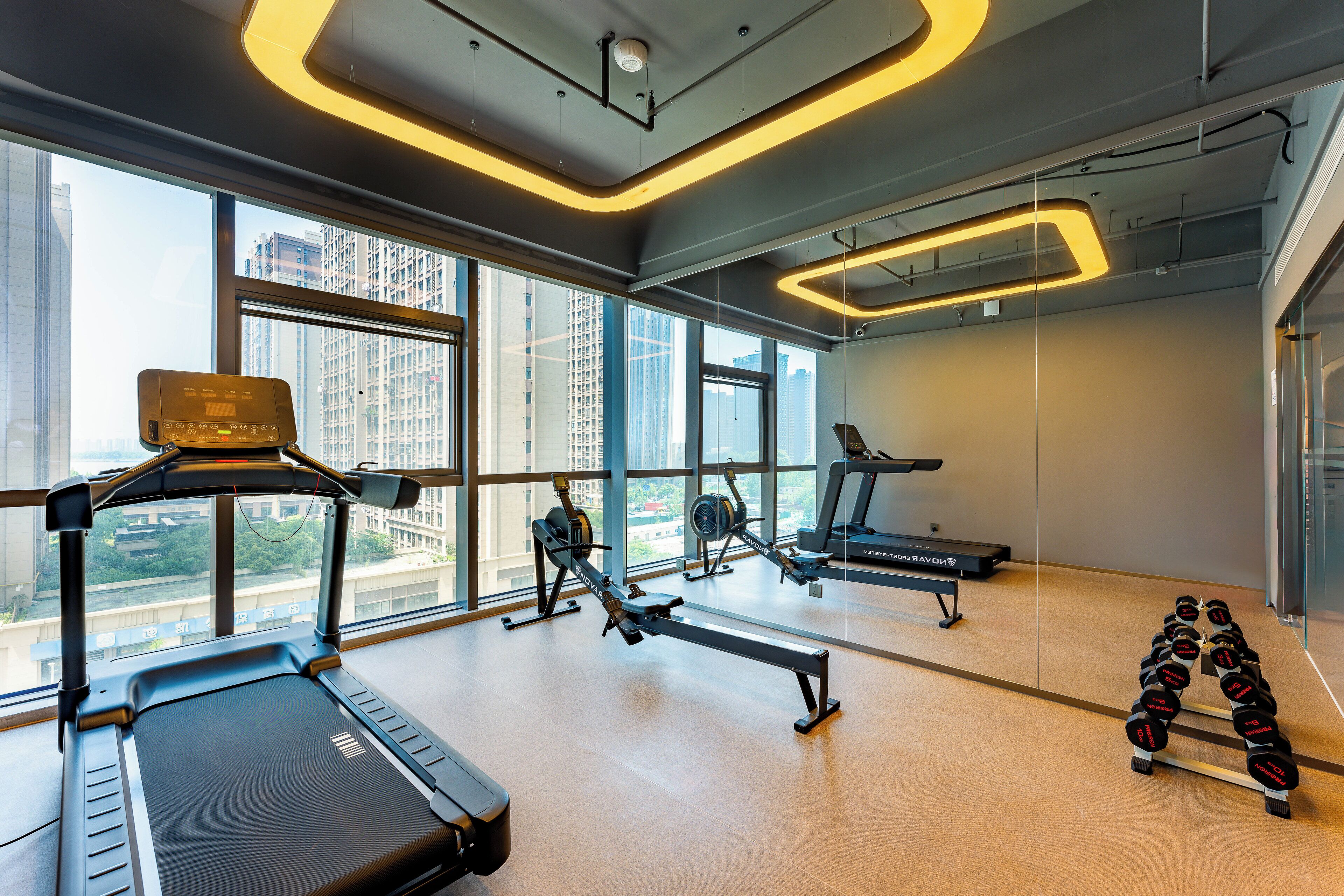A gym with treadmills, rowing machines, and dumbbells, large windows, and a modern design.
