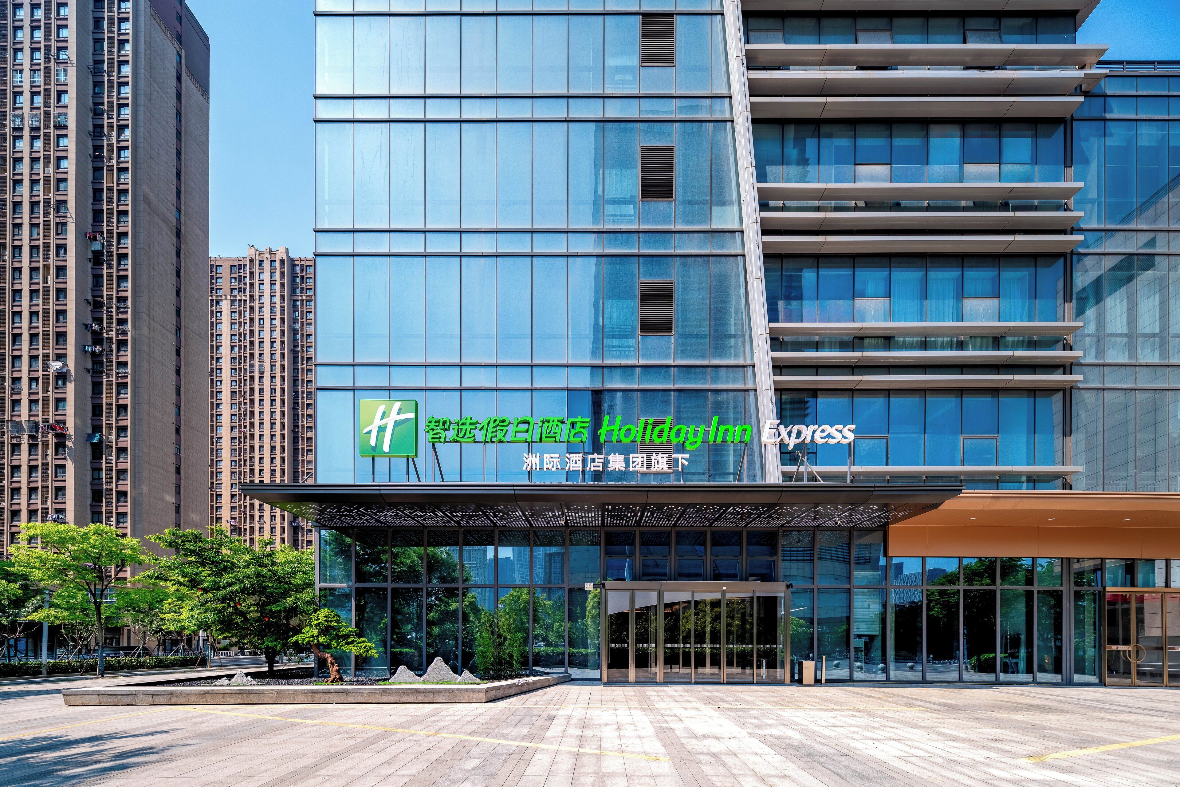 A modern hotel with a glass facade, outdoor seating area, and a clear view of the surrounding high-rise buildings.