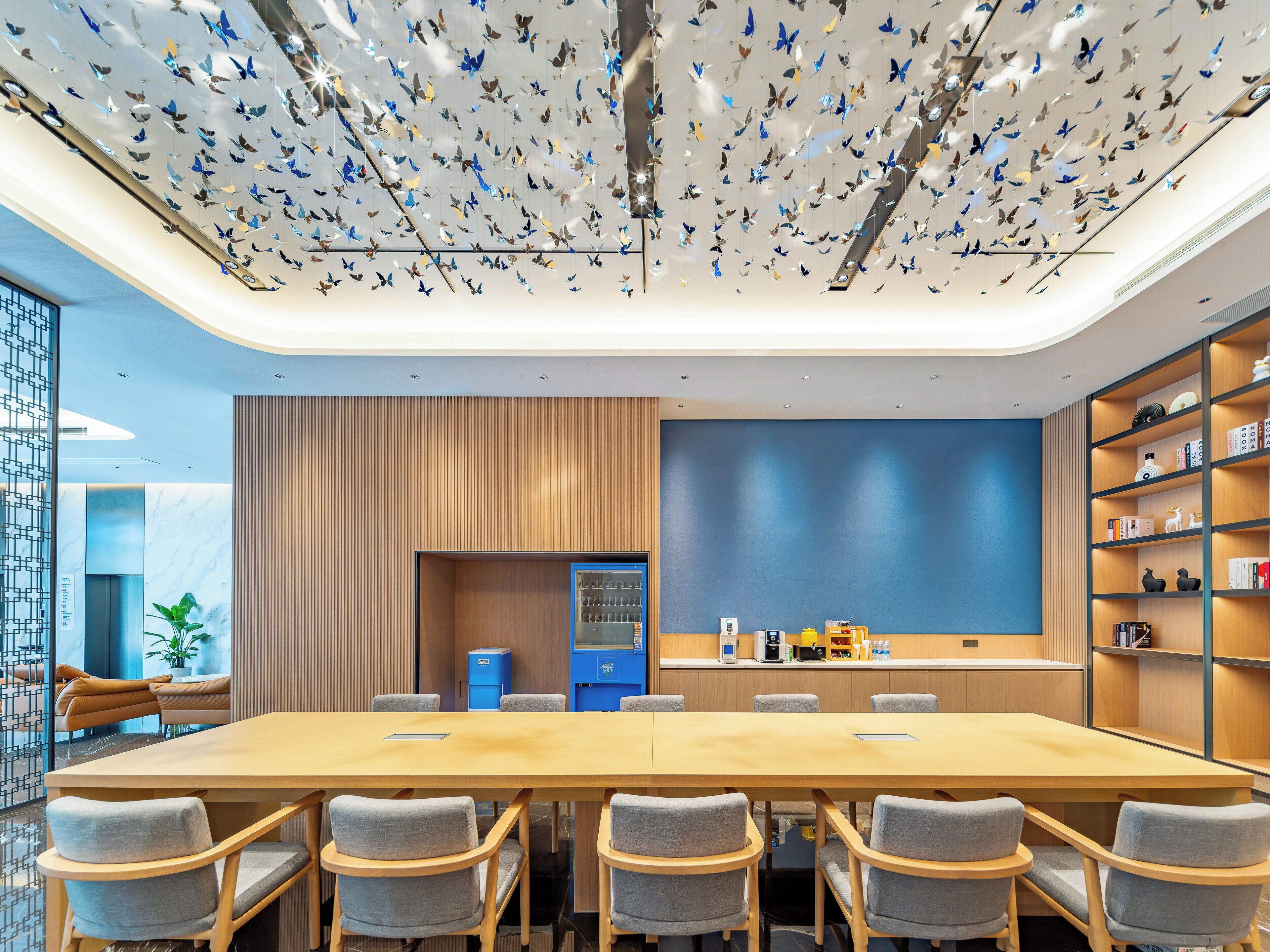 A modern meeting room with a long table, chairs, a blue accent wall, and a ceiling with hanging butterfly decorations.