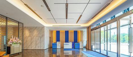 Un hall d’entrée moderne avec un sol en marbre, un comptoir d’accueil et de grandes fenêtres donnant sur l’extérieur.
