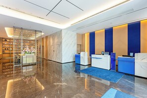 A modern reception area with marble floors, a glass partition with a floral arrangement, and a reception desk with a blue accent wall.