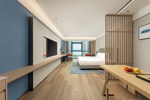 A modern hotel room with a large bed, a desk, a TV, and a view of the city.