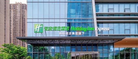 A modern hotel entrance with a glass facade, a green logo, and a sign indicating it is part of the Holiday Inn Express chain.
