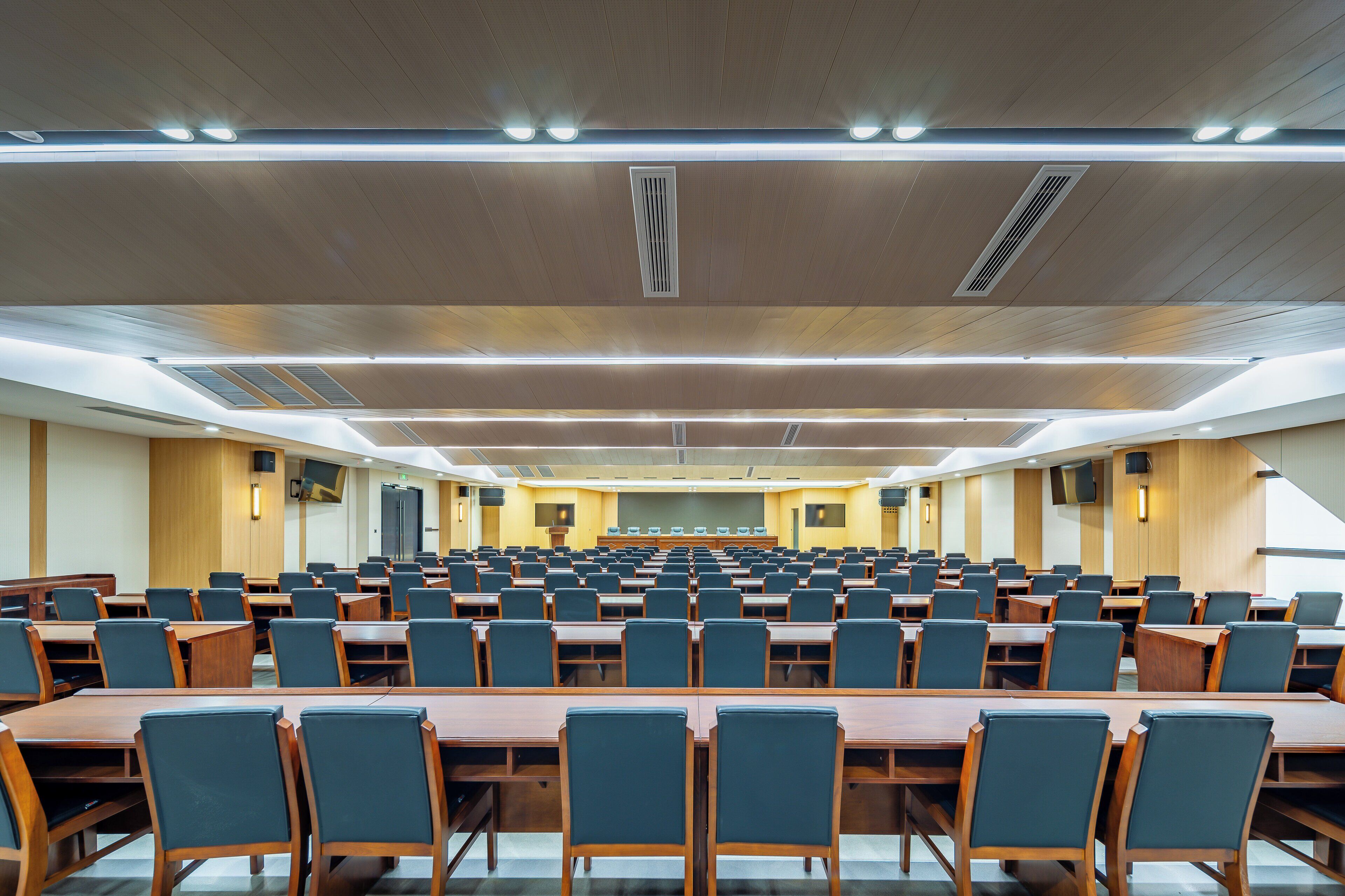 Uma sala de conferência com fileiras de mesas e cadeiras, iluminação no teto e sistema de ventilação.