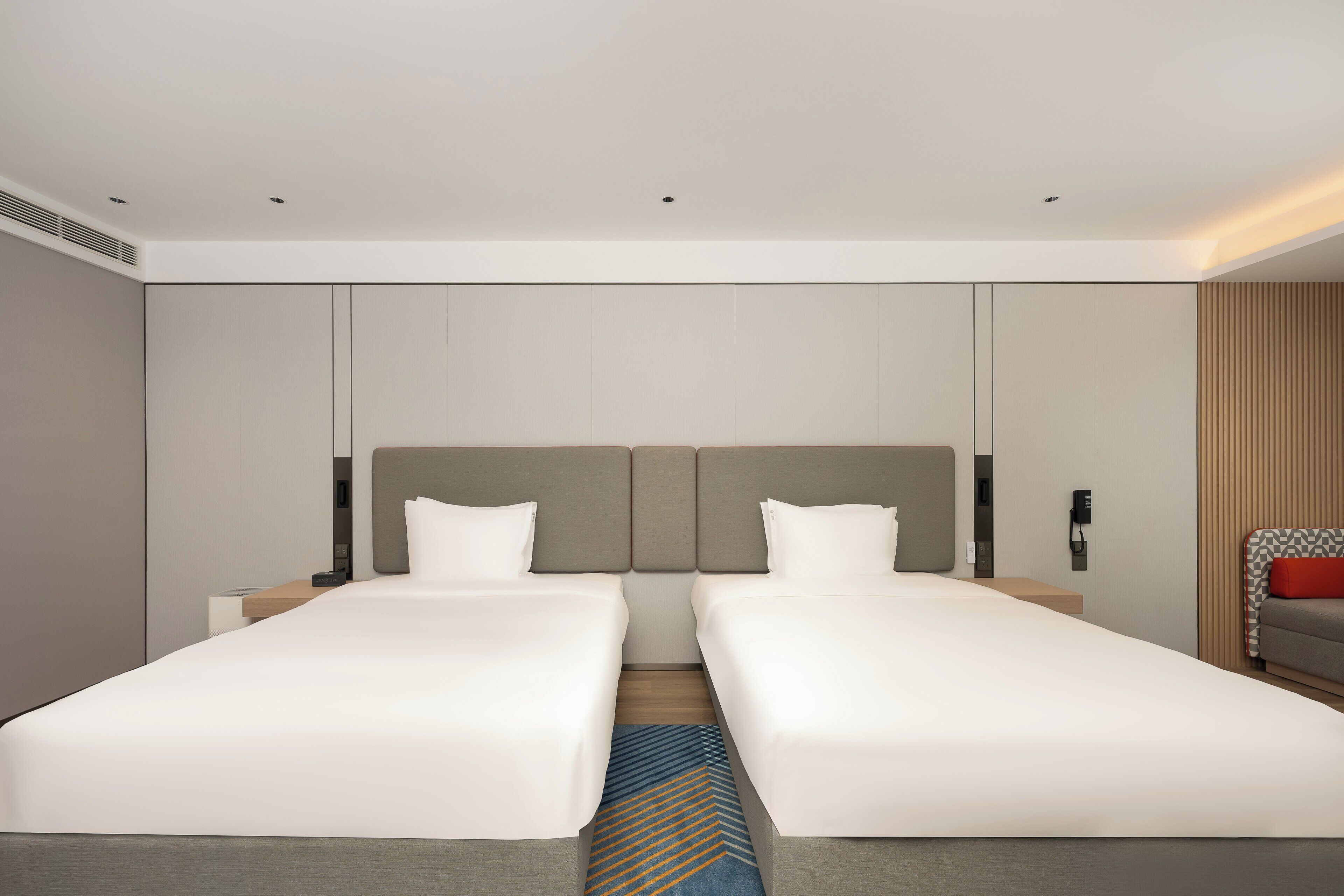 A modern hotel room with two single beds, a neutral color scheme, and a large mirror on one wall.