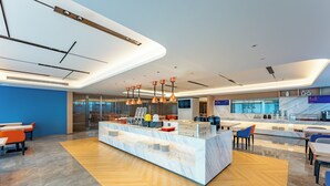 Un hall d’hôtel moderne avec un comptoir central, des espaces salon et un grand écran de télévision.