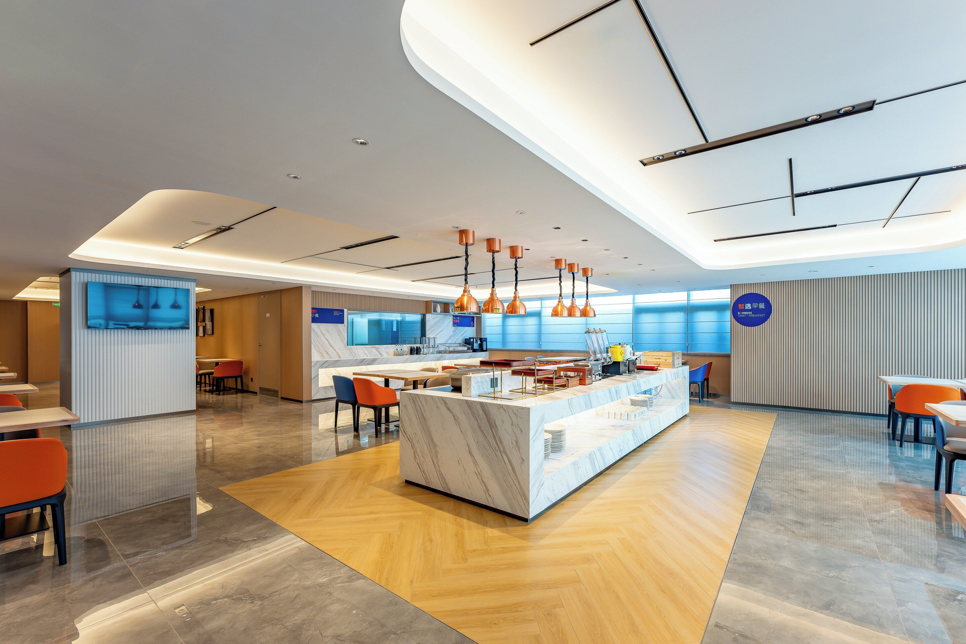 A modern hotel lobby with a marble reception desk, orange chairs, and a wooden floor.