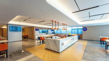 A modern hotel lobby with a marble reception desk, orange chairs, and a wooden floor.