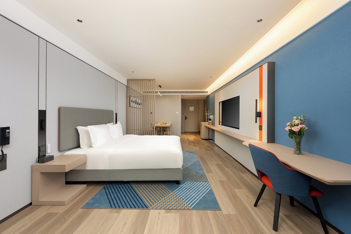 A modern hotel room with a bed, desk, and TV.