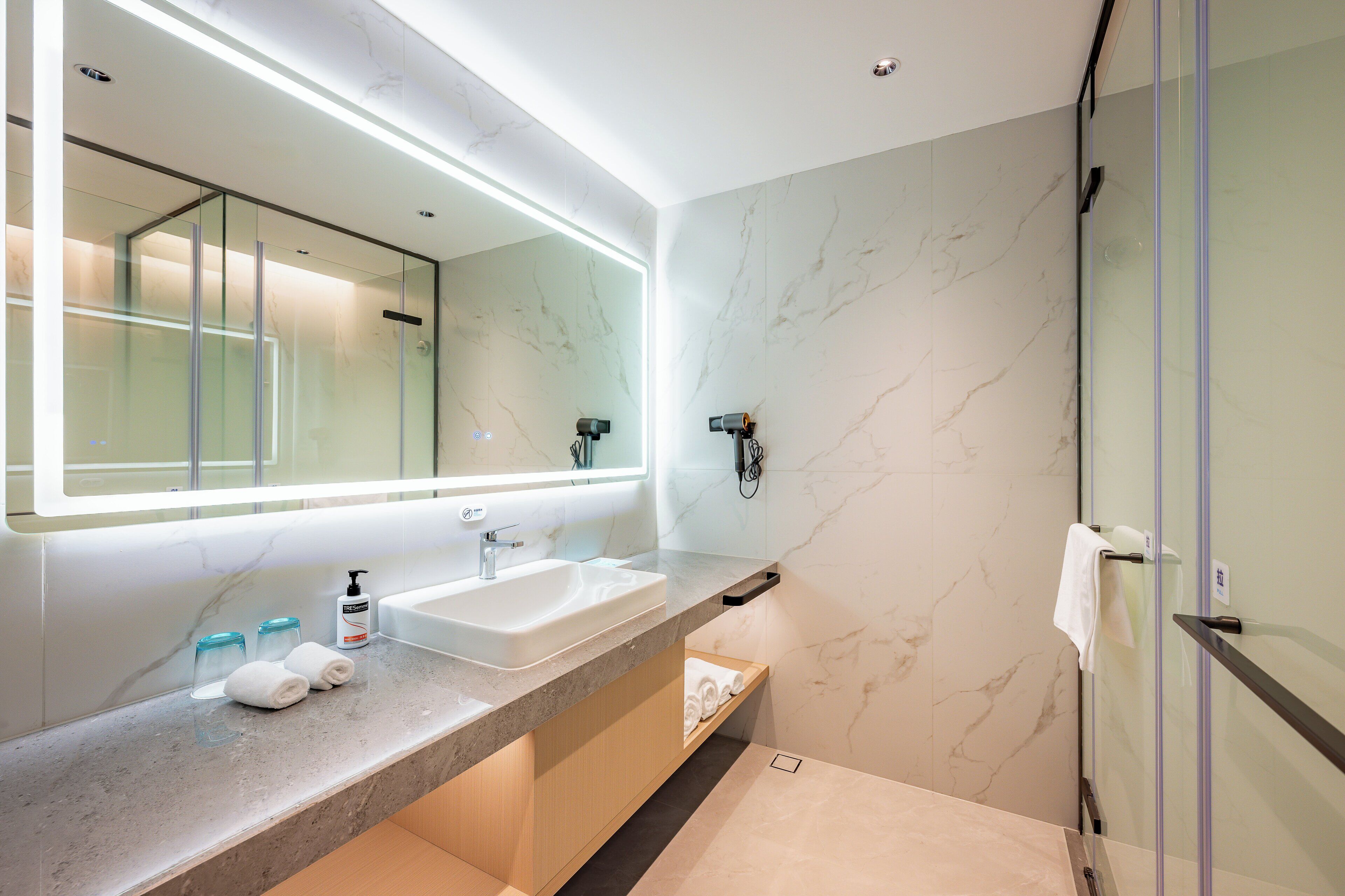 Un baño moderno con un espejo grande, un lavabo y una cabina de ducha con mampara de vidrio.