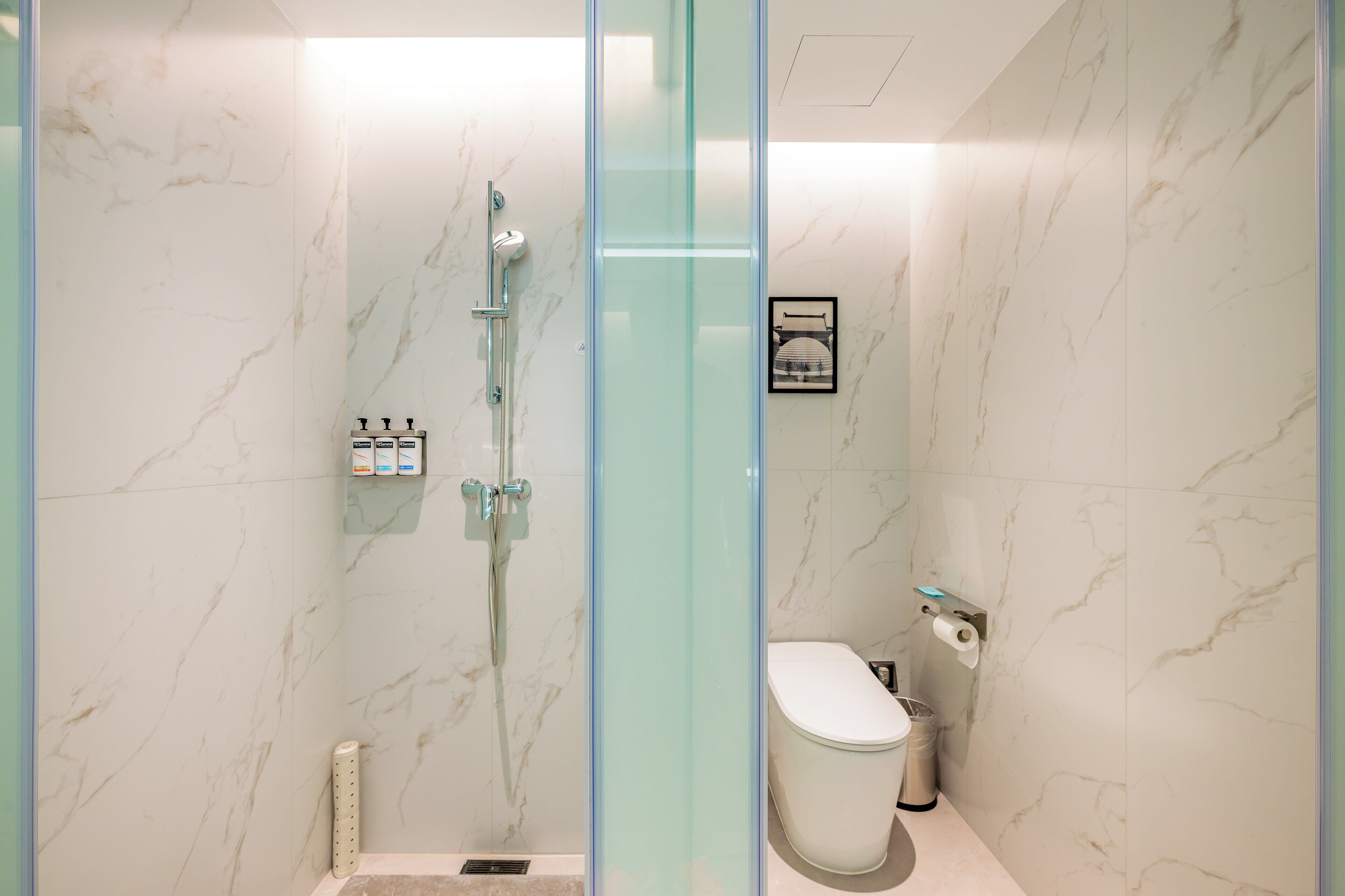 Une salle de bain moderne avec une douche à parois de verre, des toilettes et un mur en marbre.