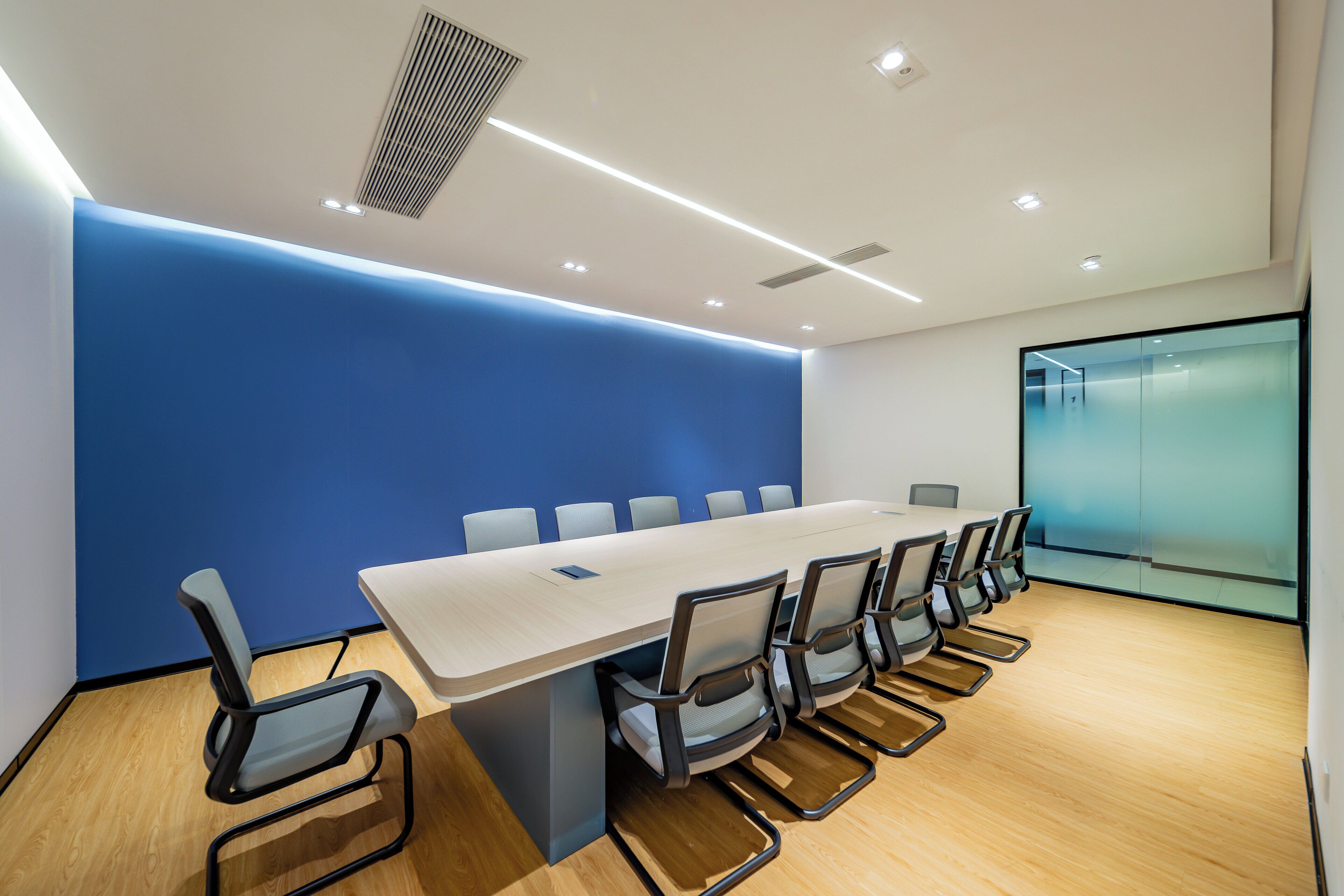 Un salón de conferencias con una larga mesa, sillas y una pared azul decorativa.