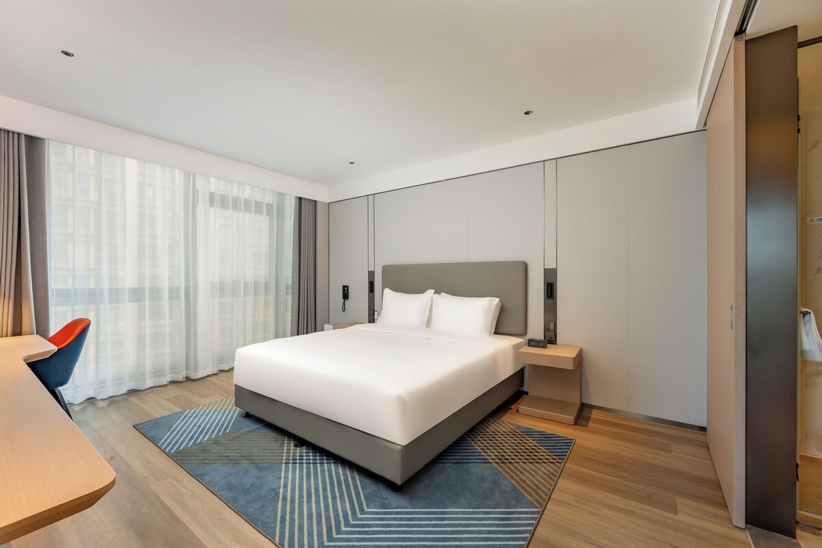 A modern hotel room with a large bed, a desk, and a chair.