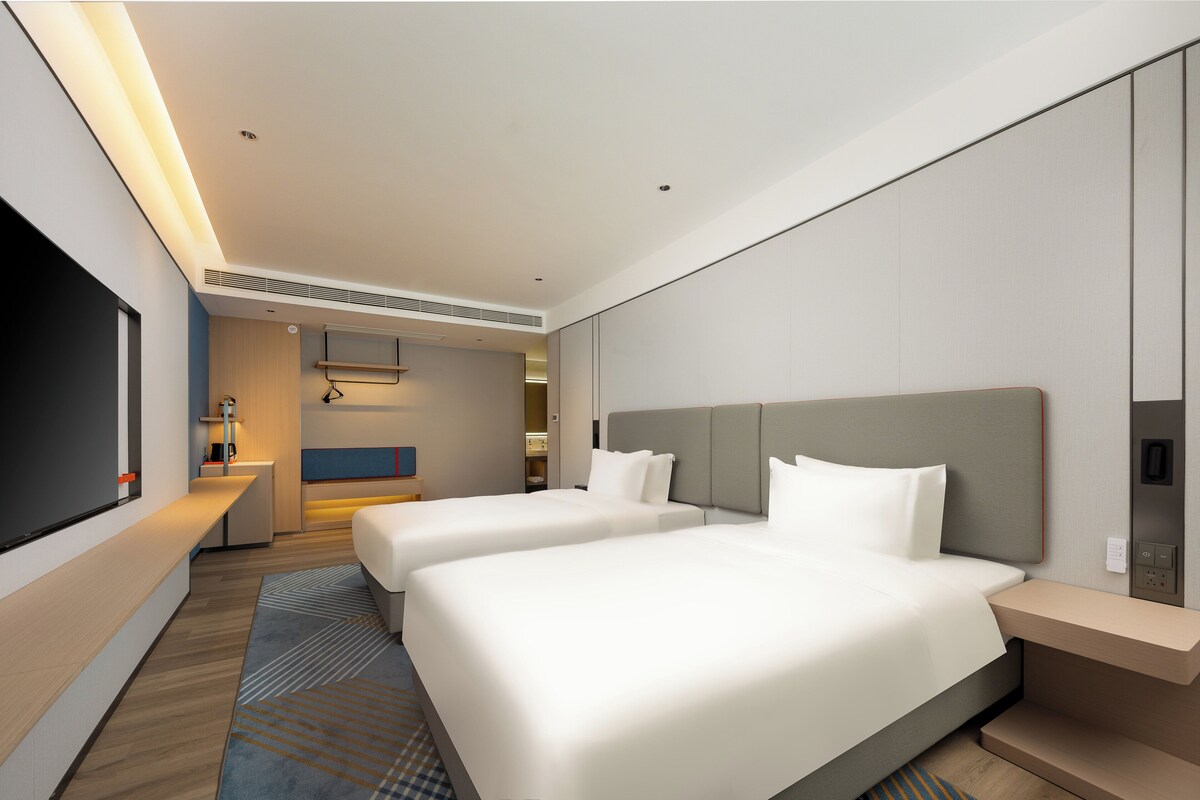 A hotel room with two beds, a TV, a desk, and a bathroom.