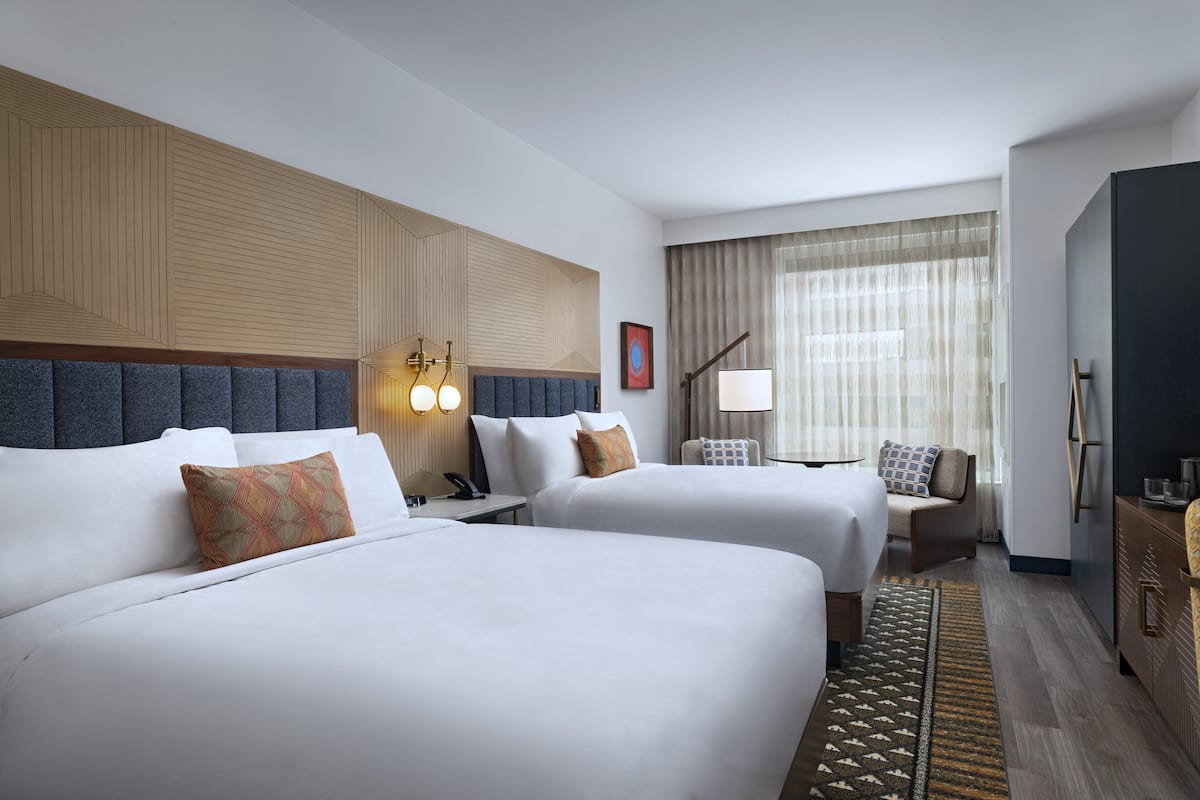 A hotel room with two beds, a desk, a chair, a lamp, and a wardrobe.