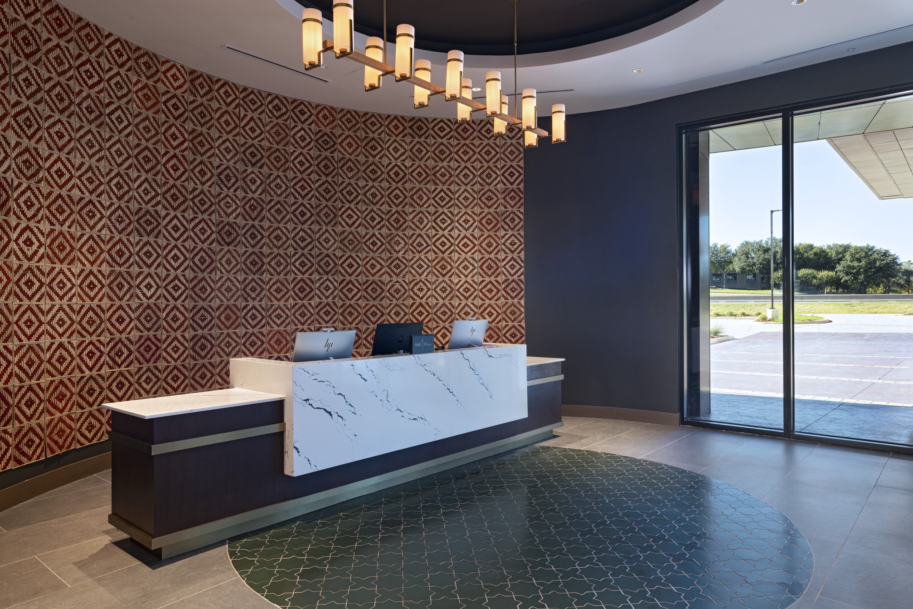 A reception area with a patterned wall, a marble counter, and a view of the outdoors through large glass doors.