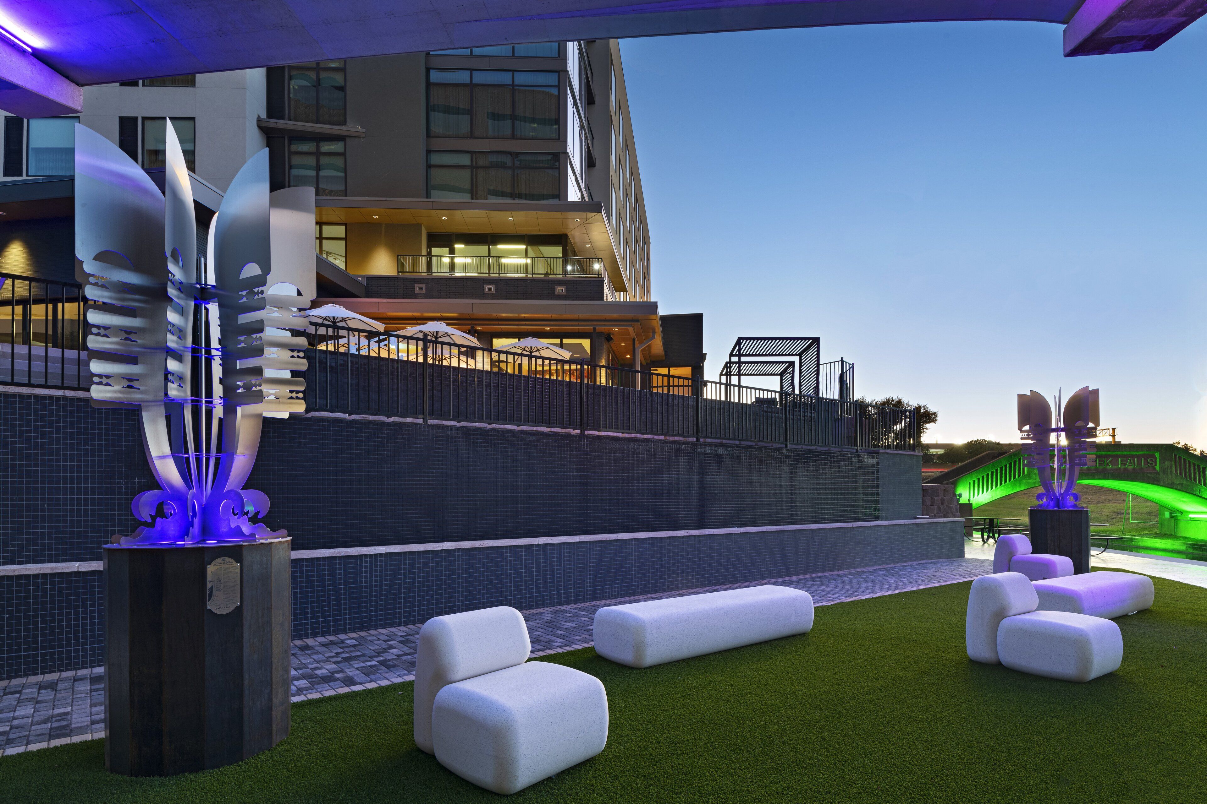 Terraza en la azotea con césped artificial, asientos blancos acolchados y esculturas modernas.