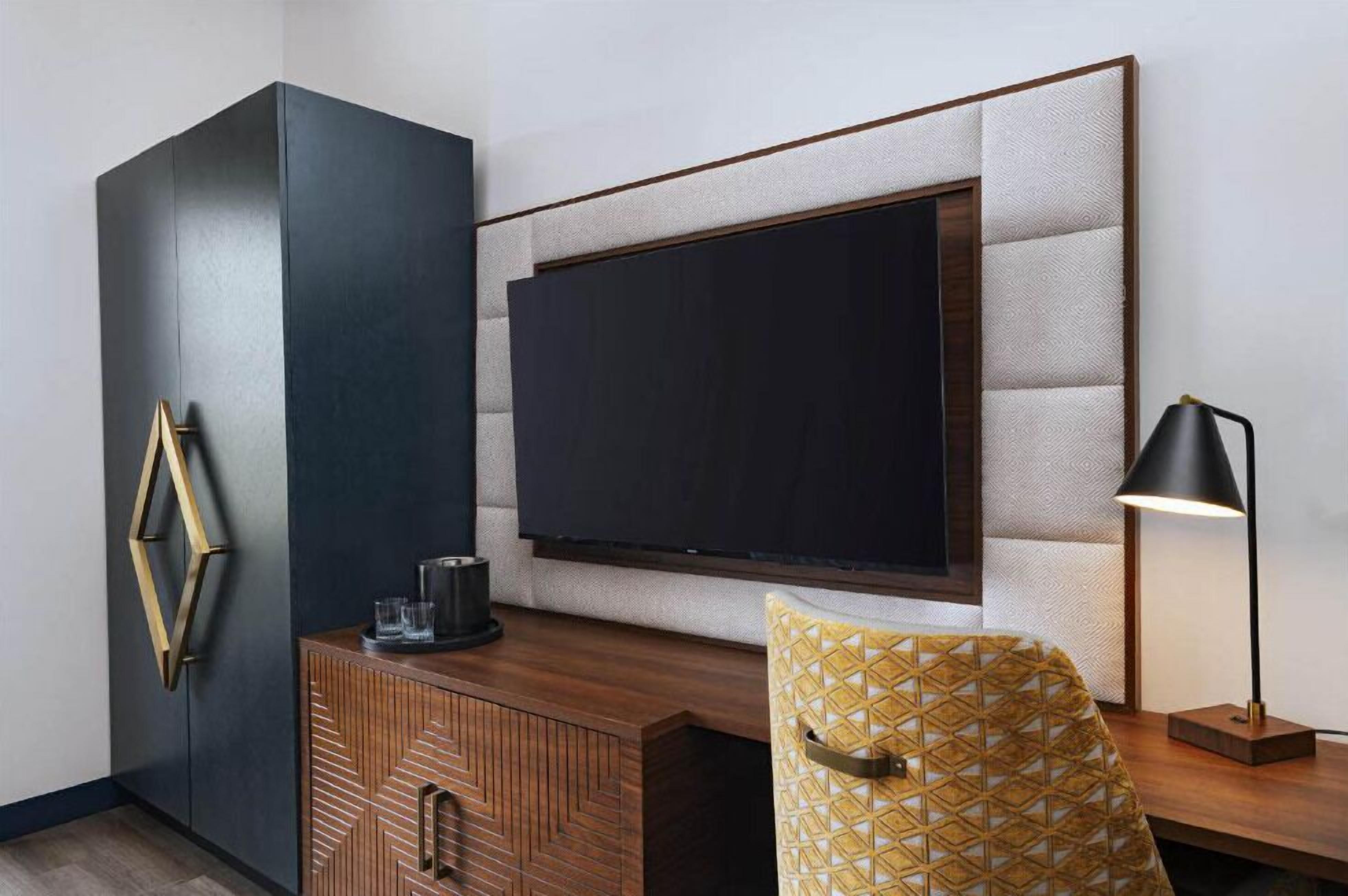 A modern room with a large flat-screen TV mounted on a textured wall, a wooden cabinet with geometric patterns, and a patterned armchair.