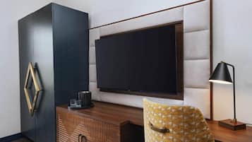 A modern room with a large flat-screen TV mounted on a textured wall, a wooden cabinet with geometric patterns, and a patterned armchair.