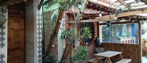A rustic outdoor seating area with a wooden table and benches, surrounded by potted plants and a decorative metal gate.