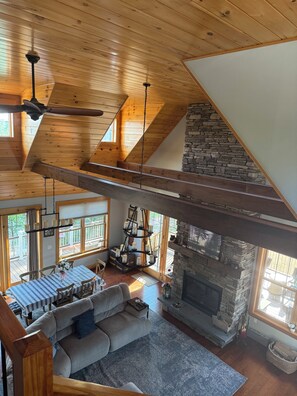 A spacious loft-style room with a stone fireplace, wooden beams, and a dining area with a blue tablecloth.
