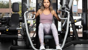 Une personne utilise un appareil de musculation pour les jambes dans une salle de sport, où se trouvent divers autres équipements d'exercice.