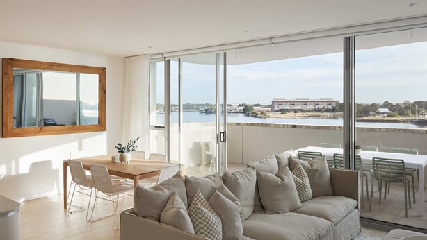 A modern living room with a large sliding glass door leading to a balcony with a view of a marina and buildings.