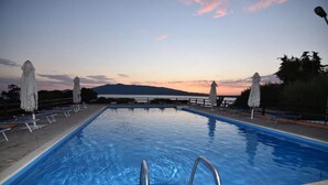 A swimming pool with lounge chairs and umbrellas, surrounded by a wooden deck and a mountain in the background. - Tuscany, Ansedonia - Villa for 7 people with swimming pool (Ansedonia)