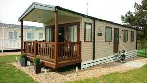 A mobile home with a wooden deck, a covered porch, and a small staircase leading to the entrance. - Lovely 2-bedroom Lodge set in Beautiful Norfolk (Great Yarmouth)